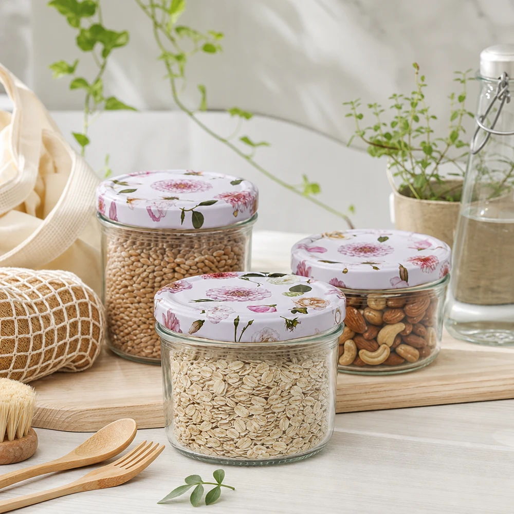 Cilindrische pot 230 ml + deksel BasicSeal roze bloem Drie 230 ml cilindervormige potten met roze bloemendeksels gevuld met granen en noten in een duurzame keukenomgeving
