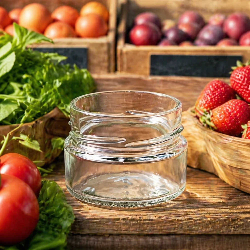 80ml rond glas zonder deksel (TO58deep) UNiTWIST UNiTWIST Runda80 ronde pot 80ml TO58deep lege inmaakpot op houten tafel met vers fruit en groenten op de achtergrond