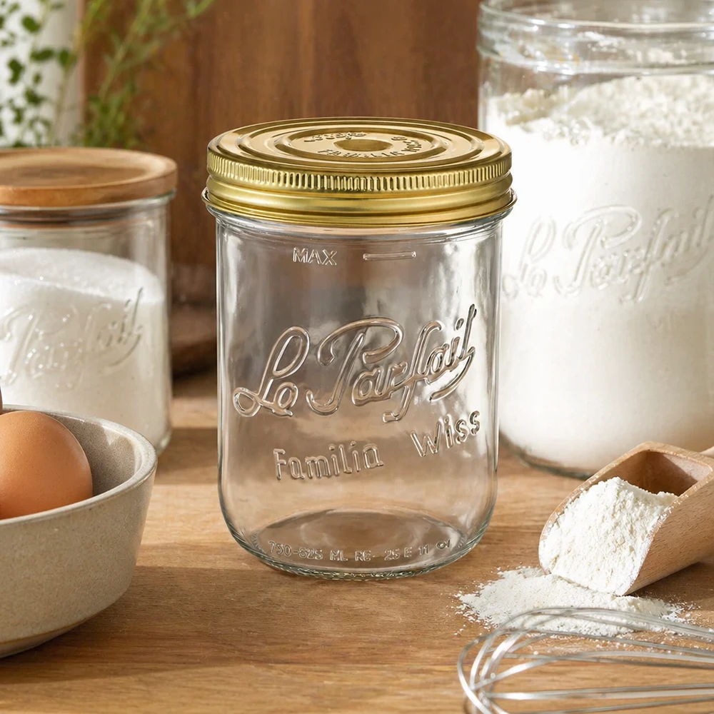 Le Parfait® Familia Wiss 1 kg Ø100 mm pot 1020ml Familia Wiss pot met gouden deksel op houten tafel naast bakingrediënten en andere inmaakpotten
