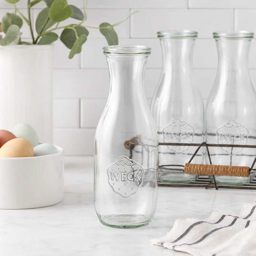 Sapfles van 1062 ml met glazen deksel WECK RR60 WECK sapfles 1062ml glazen fles leeg in moderne witte keuken met eierschaal draadmand en plant