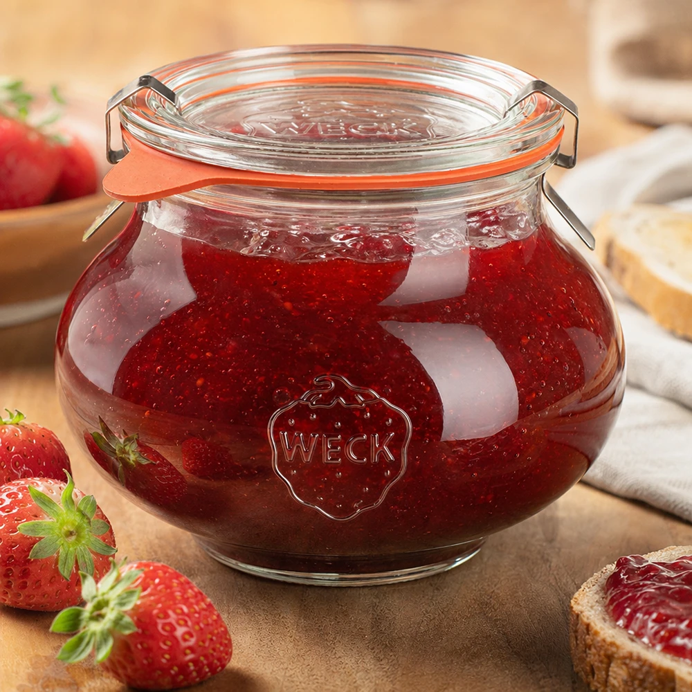 560 ml sierglas, compleet WECK RR80 WECK decoratieve pot 560ml gevuld met zelfgemaakte aardbeienjam, klapdeksel gesloten, omringd door vers fruit en groenten.