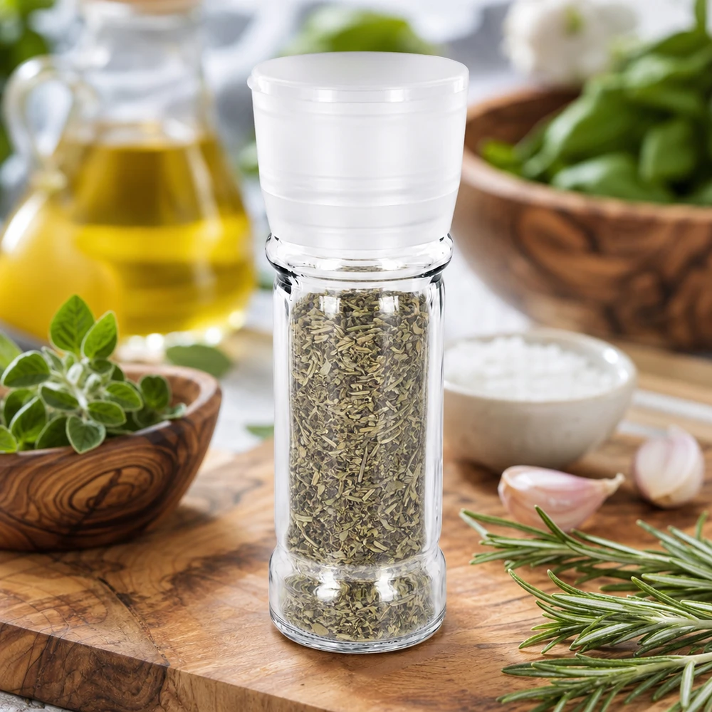 Zoutmolen van 100 ml van helder glas met een witte maalkop, tussen mediterrane ingrediënten en basilicum